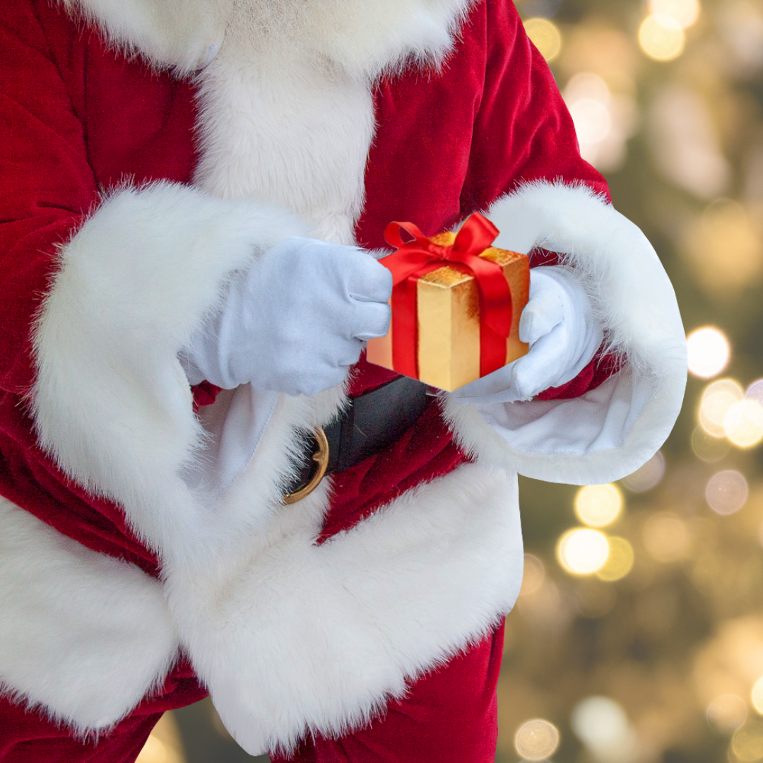 Santa Claus holding a small gold gift box with a red ribbon, against a blurred background of festive lights. The scene conveys warmth and holiday cheer.